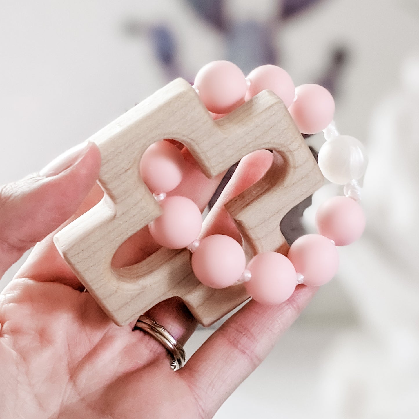 Hand holding pink and pearl silicone bead rosary teether