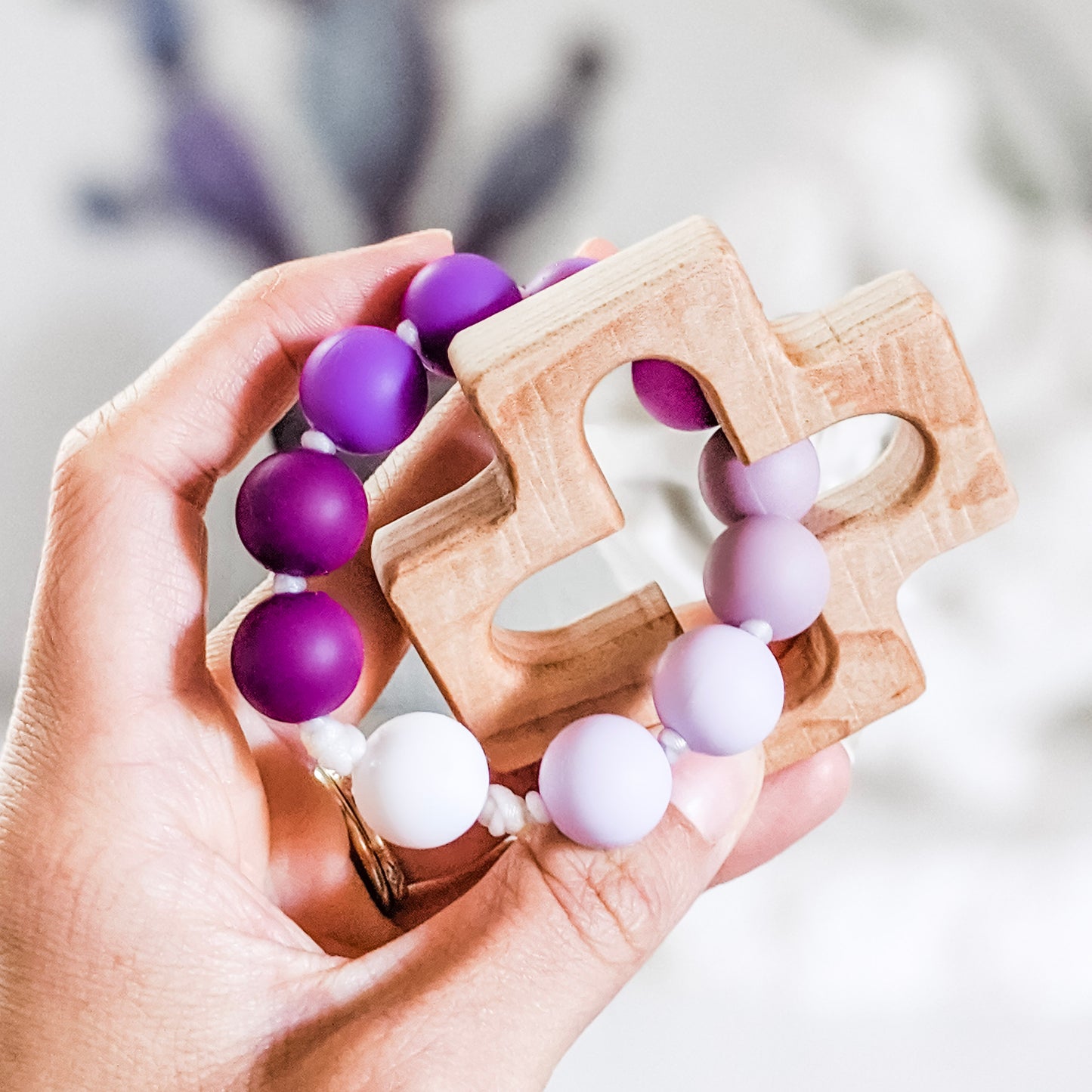 Hand holding a teething rosary made from purple silicone beads and a wooden cross teether