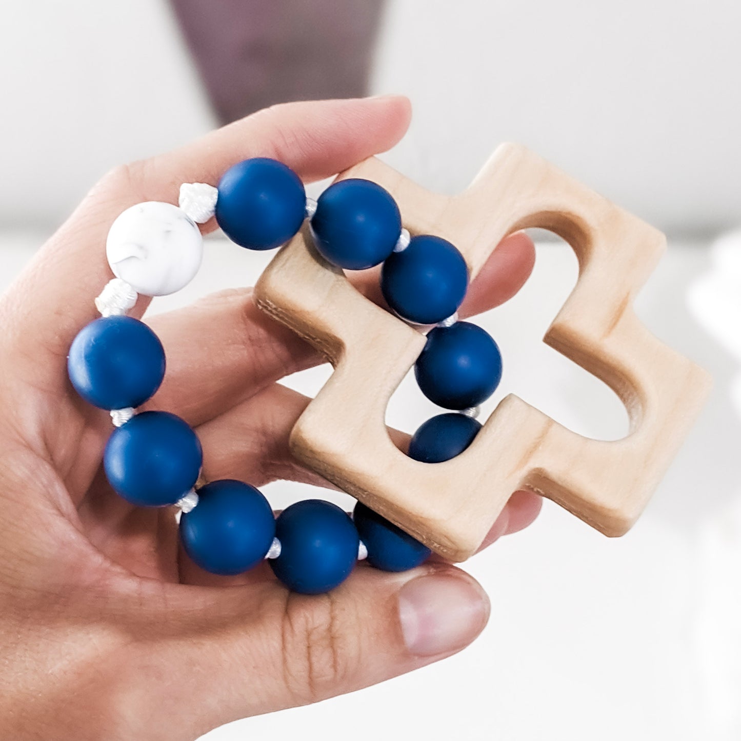 Hand holding blue and white teething rosary ring