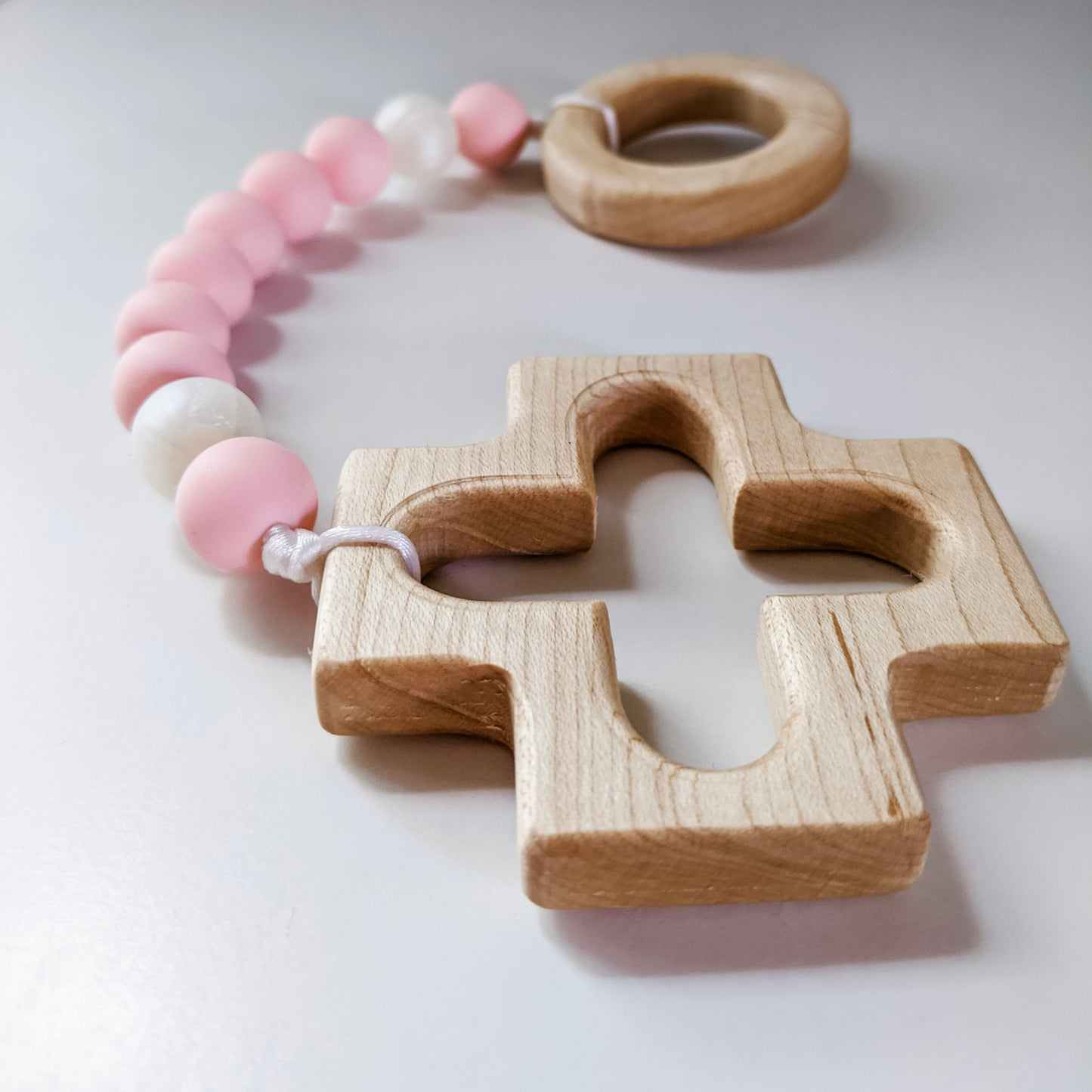 Close up of wooden cross teether from pink and pearl teething rosary