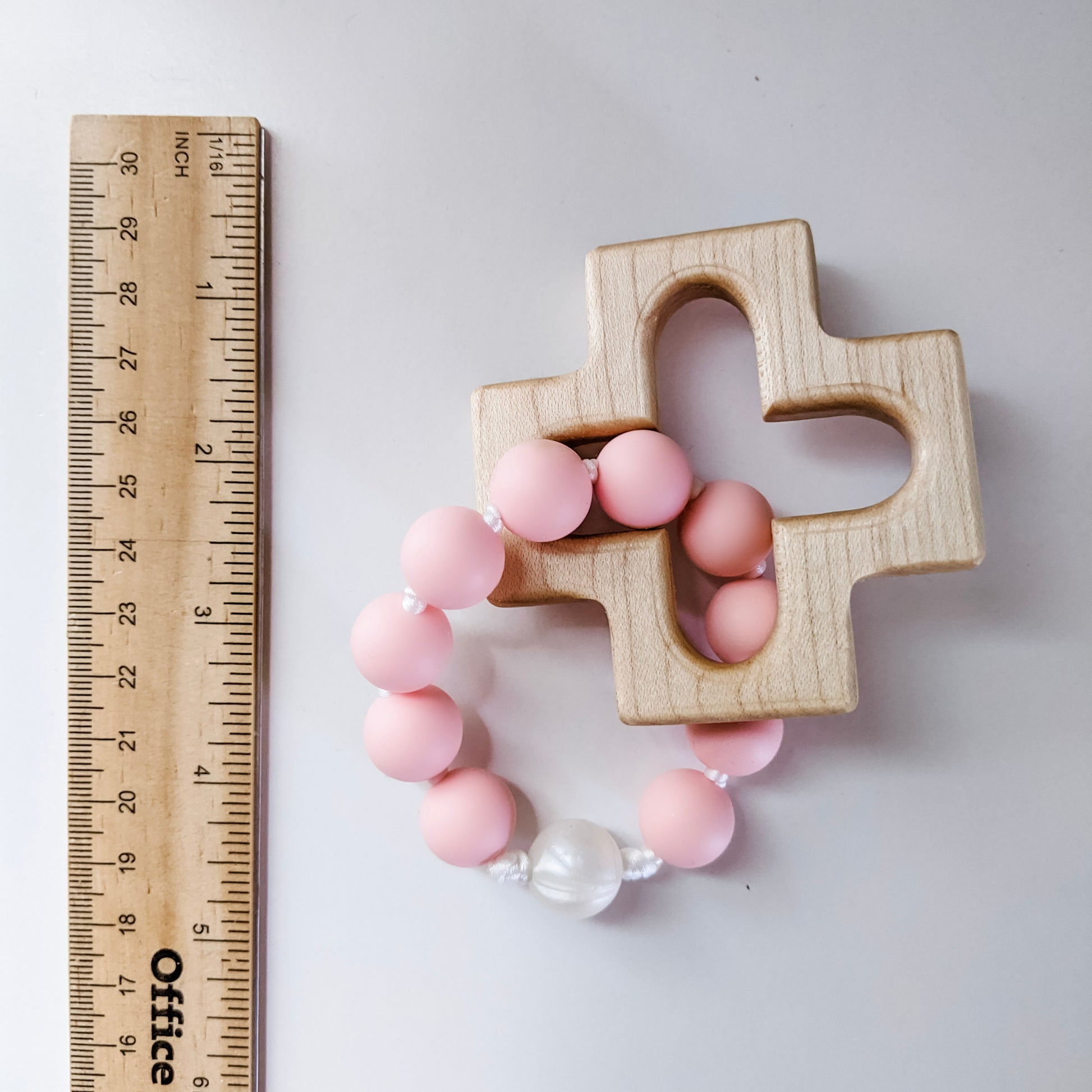 Pink and pearl silicone rosary teether next to ruler 