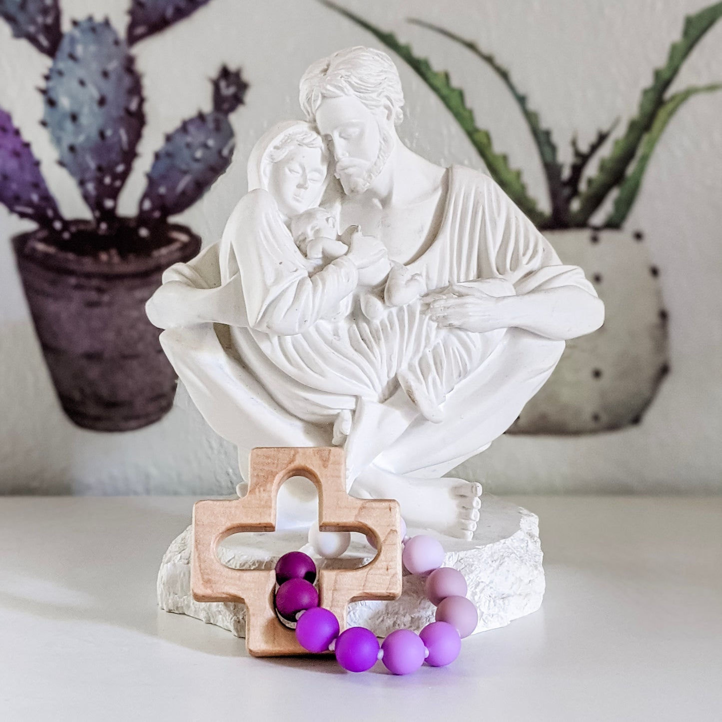 Purple rosary decade ring in front of white statue of the Holy Family