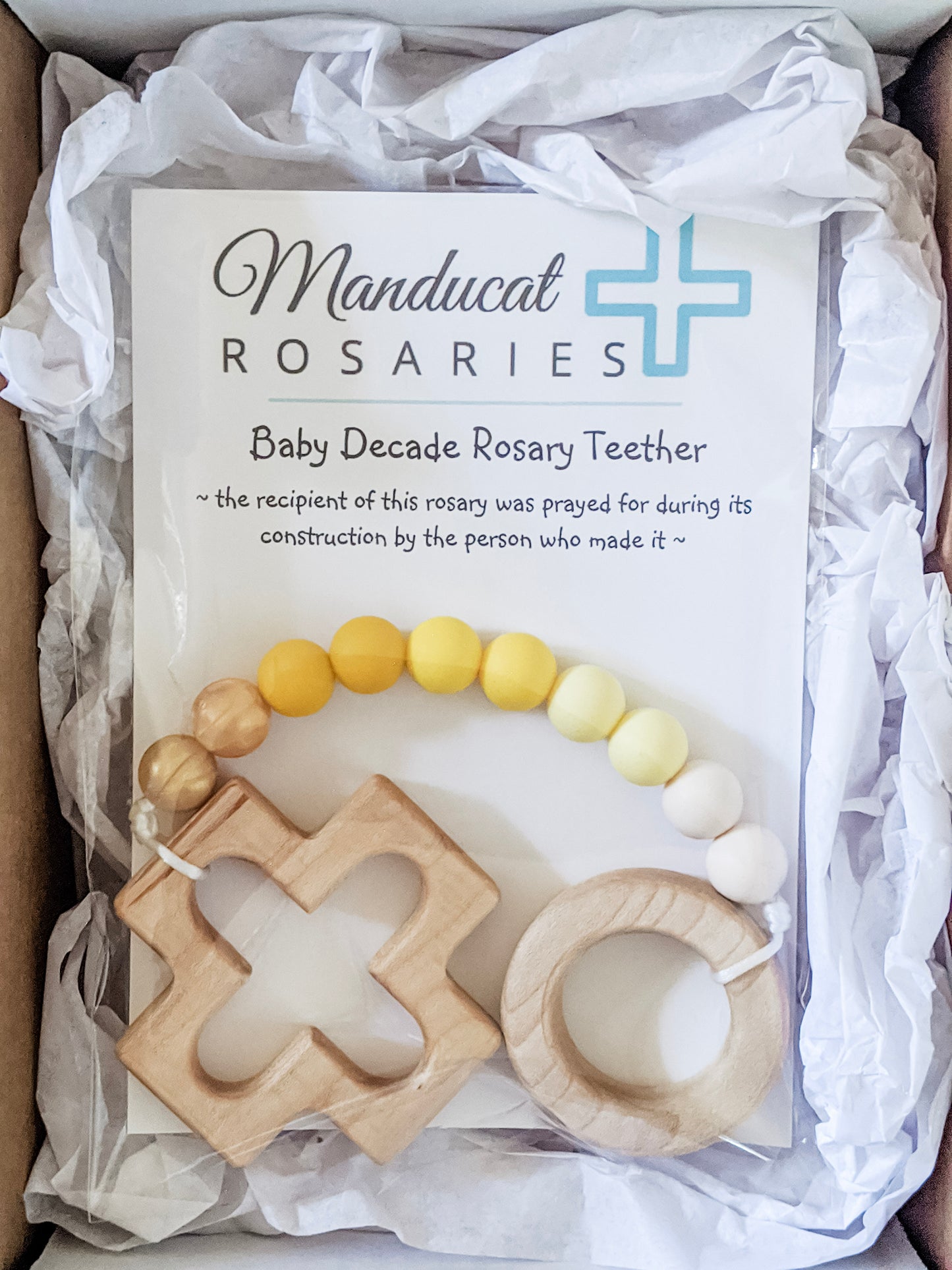 Yellow ombre teething rosary in packaging stating baby was prayed for during item's construction